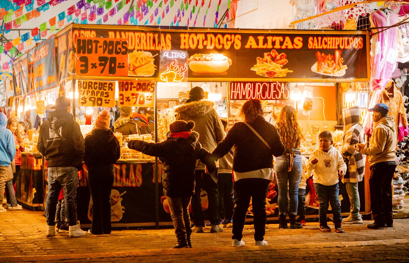 Families gathered at a festive outdoor food market with colorful decorations and community booths